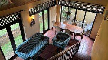 A spacious balcony with a wooden ceiling, a round dining table with chairs, and striped sofas.