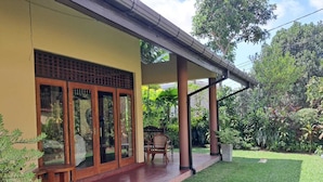 Una casa con un porche cubierto, un césped y un jardín con diversas plantas.