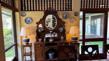 A traditional room with a wooden desk, two lamps, a mirror, and a view of the outdoors through a large window.