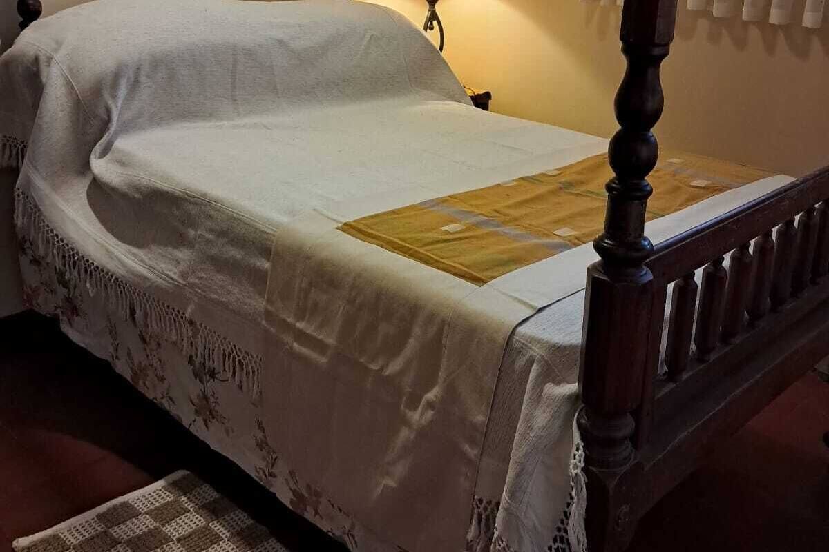 Un lit à baldaquin avec un cadre en bois, un couvre-lit blanc et une bordure en dentelle. Il y a une lampe sur une table de chevet et un tapis à motifs sur le sol.