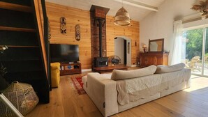 Ein gemütliches Wohnzimmer mit Sofa, Fernseher, Kamin und großen Fenstern.