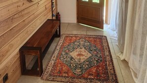 Ein Holzinnenraum mit einer Bank, einem gemusterten Teppich, einer Holztür mit Glasfeldern und einem Deckenventilator.
