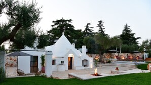 Μια λευκή βίλα με εξωτερική επένδυση από πέτρα, μια βεράντα με έπιπλα εξωτερικού χώρου και μια εστία για φωτιά.