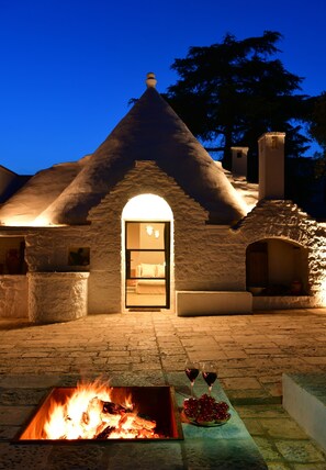 A stone building with a conical roof, a fireplace, and a table with wine glasses and fruit.