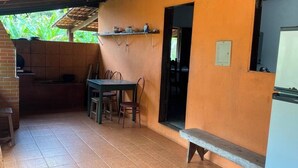 En overdækket terrasse med et bord, stole, en bagovn og et køleskab.