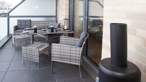 A balcony with wicker furniture, a table, and a black stove. - Above the Rooftops of Grasberg's City (Grasberg)