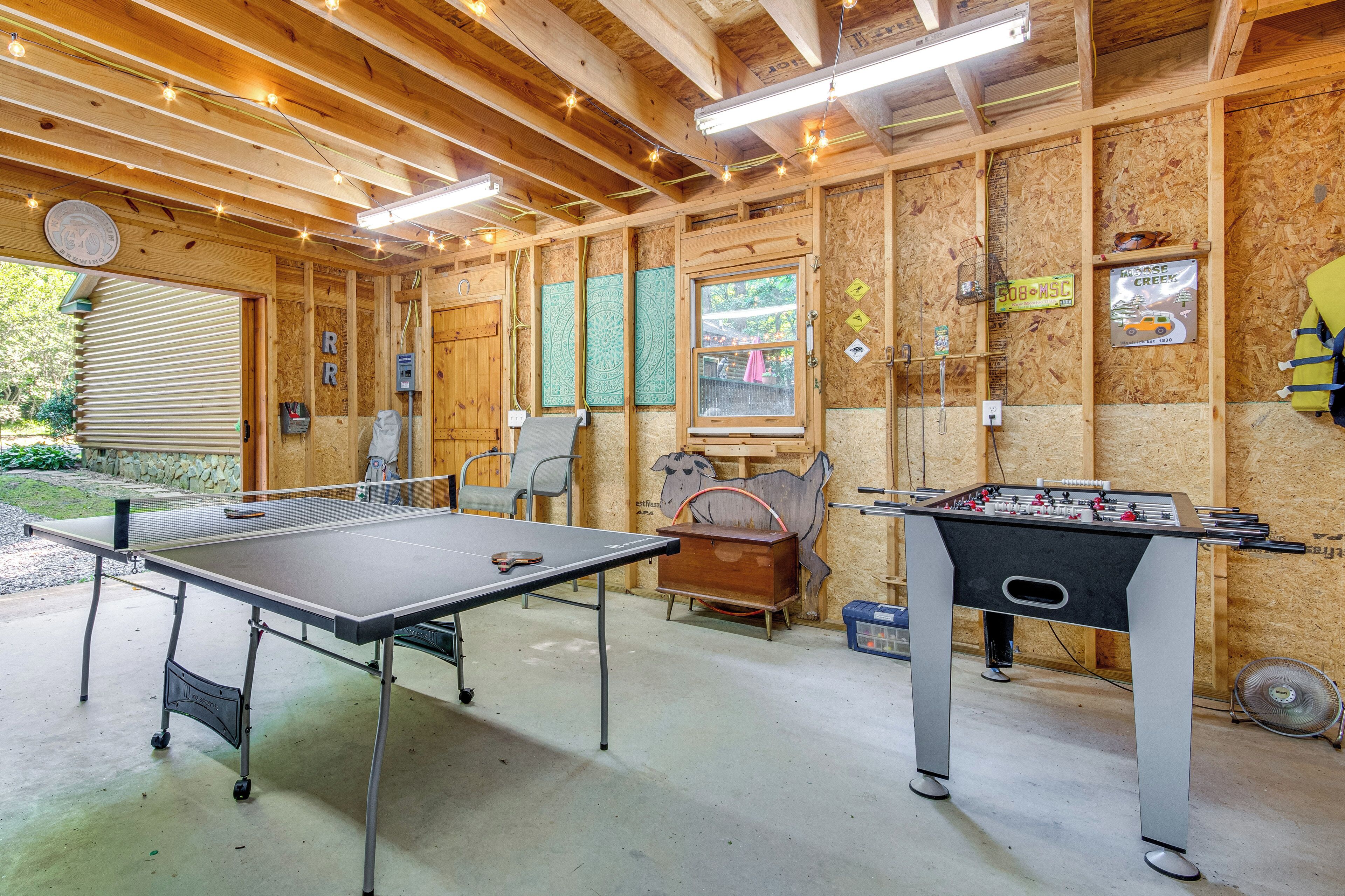 Una habitación con mesa de ping pong, mesa de fútbol de mesa y techo de madera con luces colgantes.