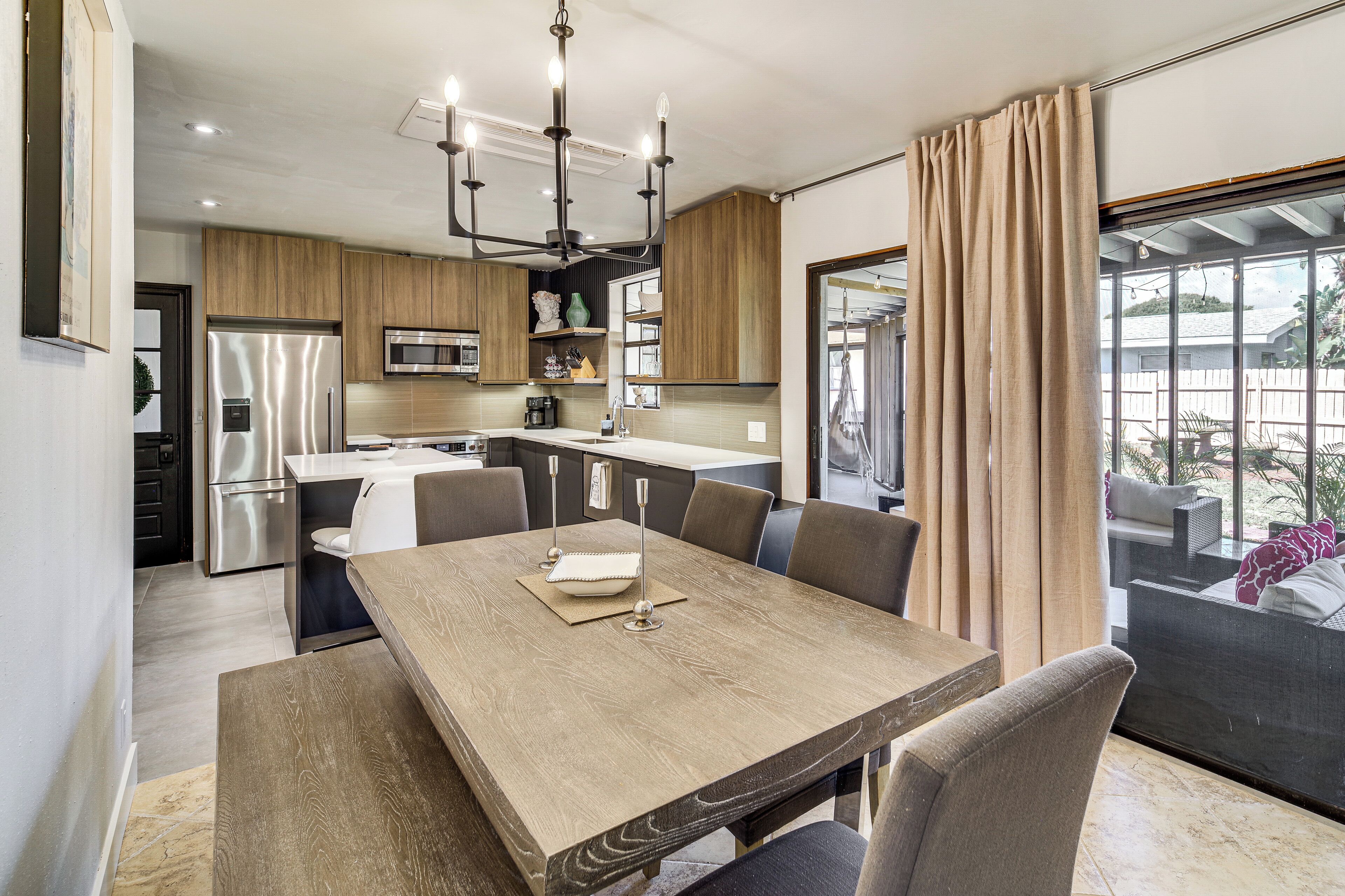 A modern kitchen with stainless steel appliances, a dining area with a wooden table and chairs, and a large window with curtains.