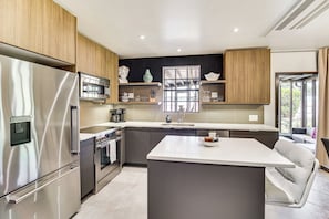 A modern kitchen with stainless steel appliances, wooden cabinets, and a large island. - 1 Block to Beach & Eats: Modern Indialantic Apt (Indialantic)