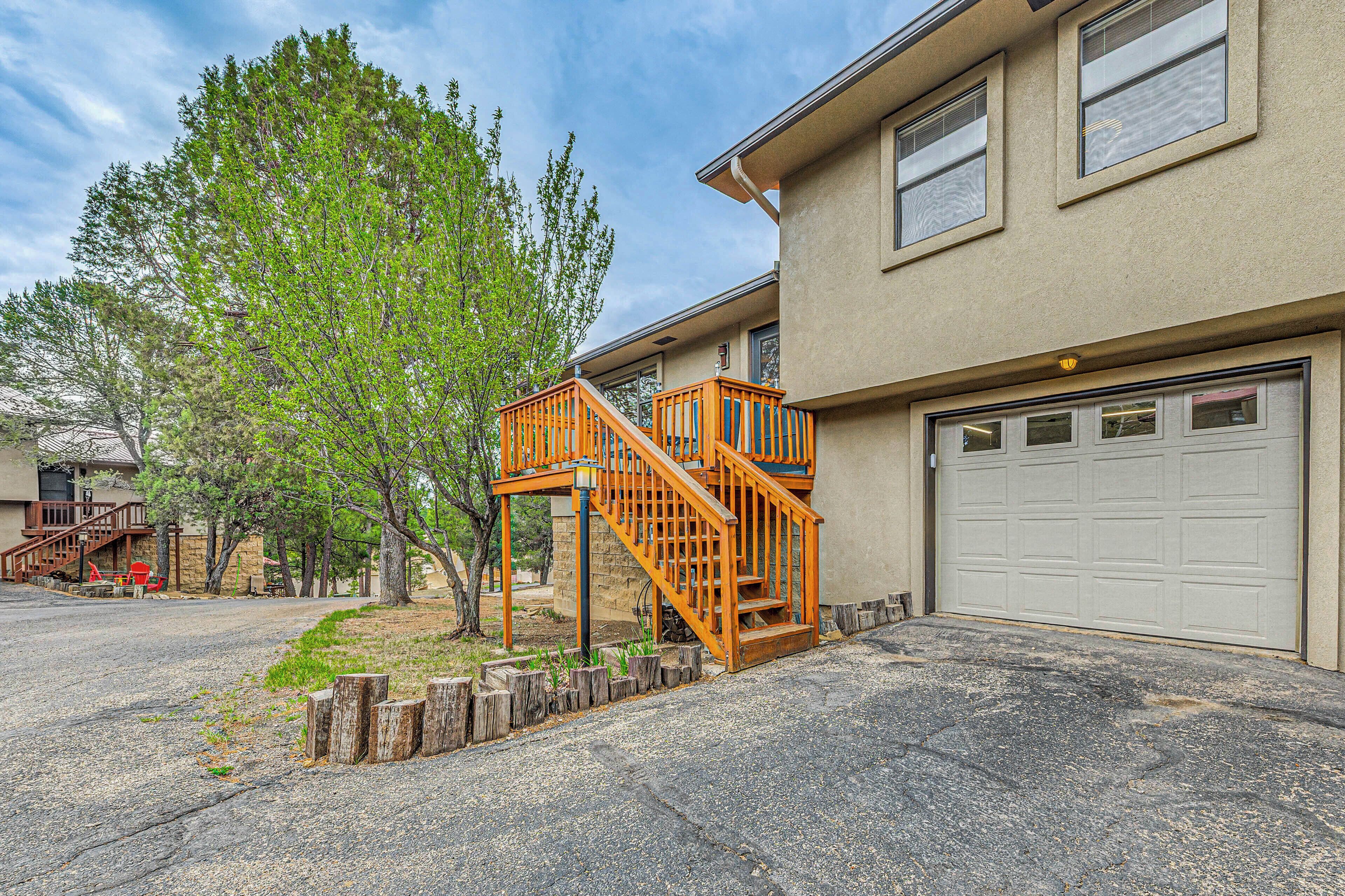 A residential building with a two-story wooden staircase leading to a deck, a garage, and a large tree in the yard.