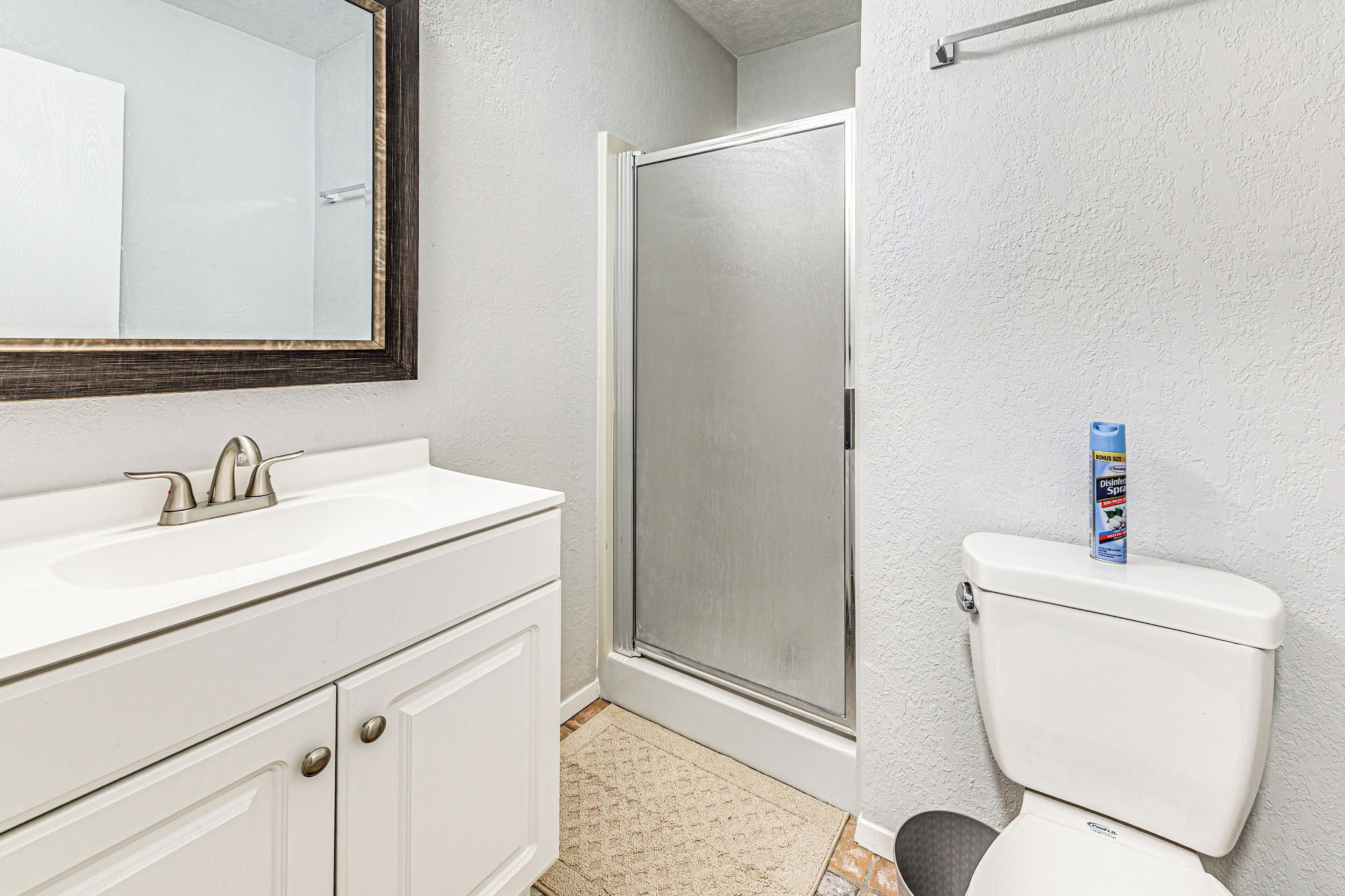 A bathroom with a white sink, a mirror, a toilet, and a shower door.