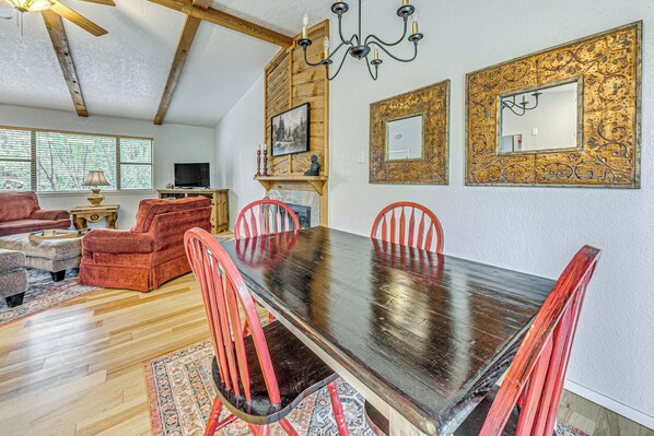 A dining area with a wooden table and red chairs, a fireplace, and a television in the background. - 4 Mi to Dtwn: Cozy Family Condo in Ruidoso! (Ruidoso)