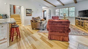A spacious living area with a wooden floor, a red sofa, a grey couch, and a kitchen area with a marble countertop and red stools. - 4 Mi to Dtwn: Cozy Family Condo in Ruidoso! (Ruidoso)