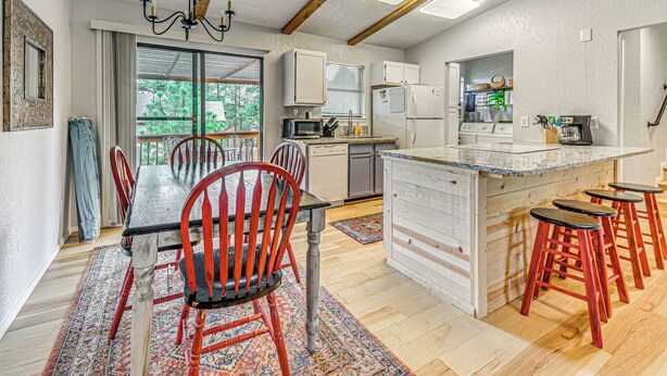 A modern kitchen with a central island, red bar stools, and a dining area with a red chair and table. - 4 Mi to Dtwn: Cozy Family Condo in Ruidoso! (Ruidoso)