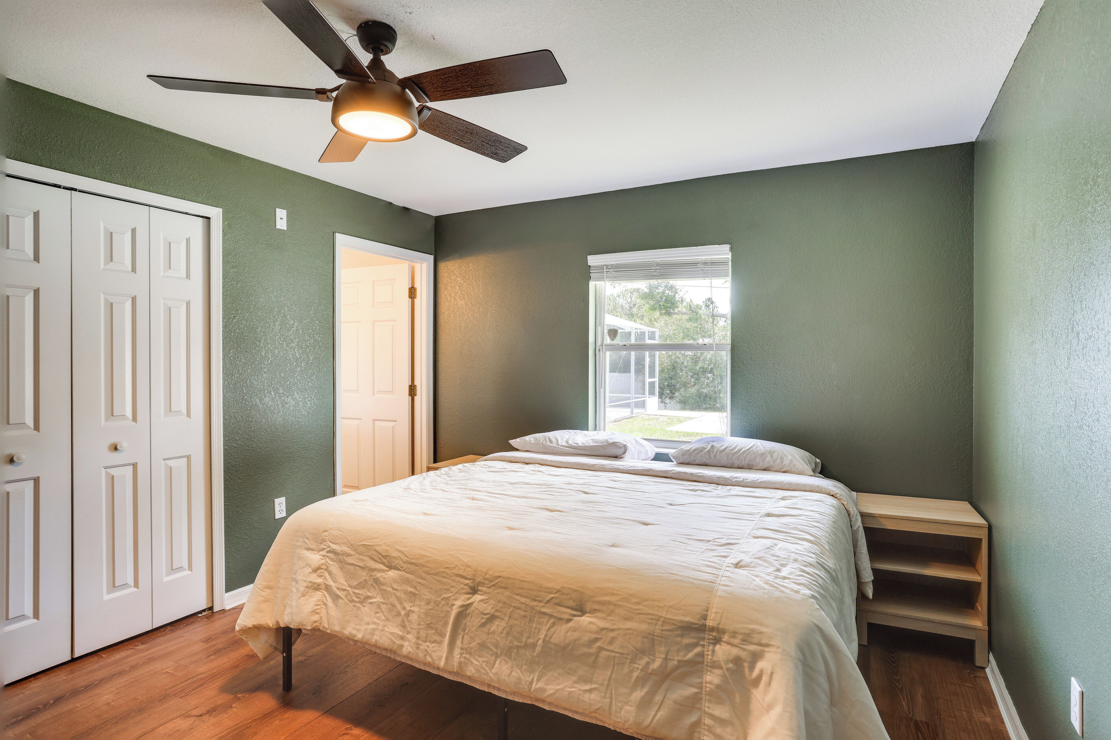 Une chambre à coucher avec un lit, un ventilateur de plafond, une fenêtre et une porte.