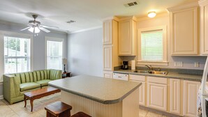 A kitchen with a central island, white cabinetry, and a green sofa in a living area. - 7 Mi to Ole Miss: Quiet Rural Retreat w/ Yard! (Oxford)