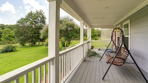 A covered porch with a swing chair, a view of a green lawn, and a wooden deck. - 7 Mi to Ole Miss: Quiet Rural Retreat w/ Yard! (Oxford)
