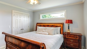A bedroom with a wooden bed, white bedding, a nightstand with a lamp, and a window with a view of greenery. - 7 Mi to Ole Miss: Quiet Rural Retreat w/ Yard! (Oxford)