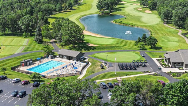 En golfbana med en swimmingpool, en parkeringsplats och en byggnad med en flaggstång.