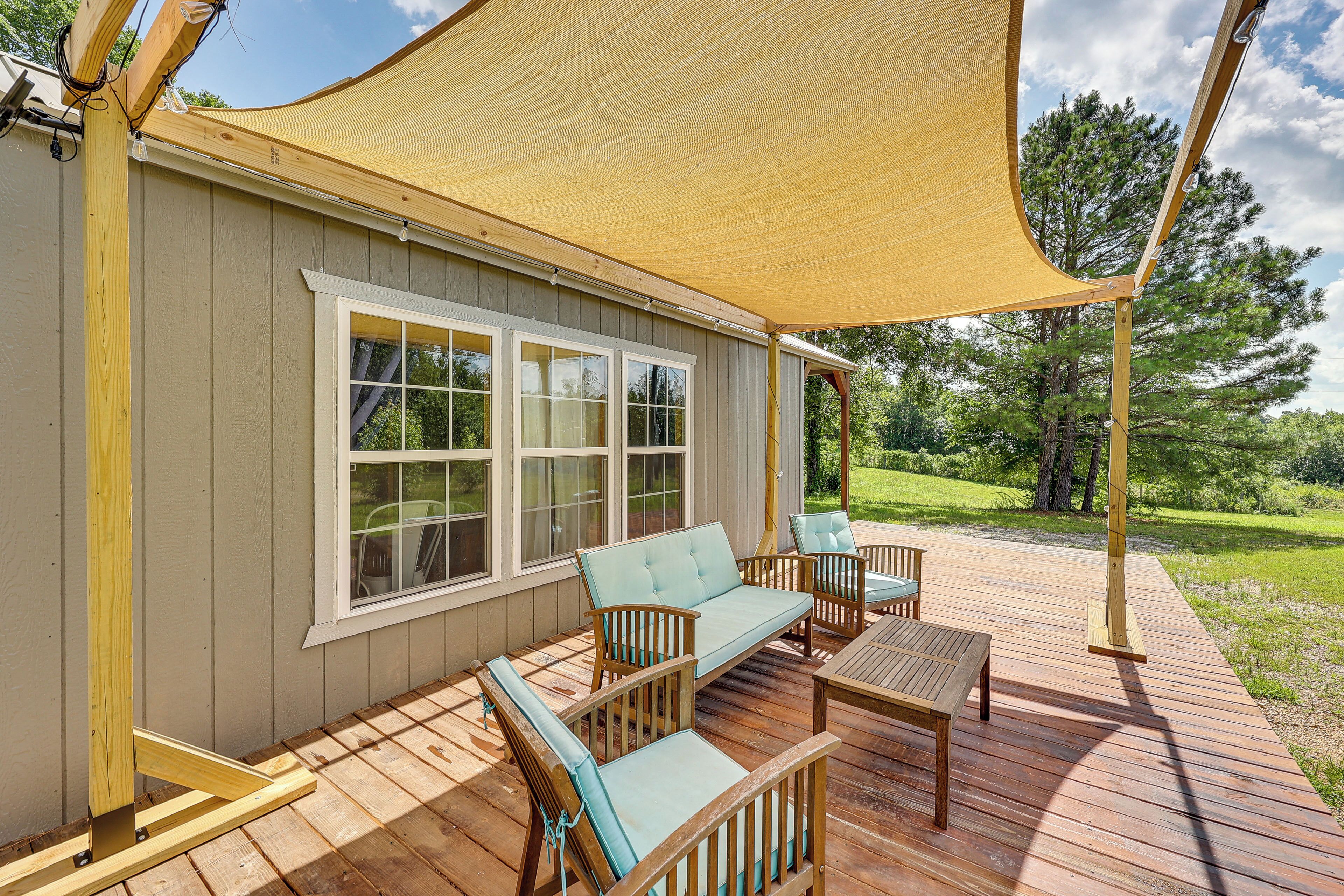 A covered deck with outdoor furniture, a large window, and a view of the surrounding landscape.