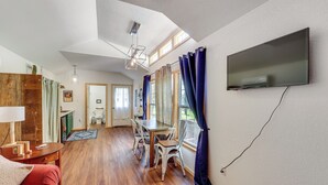 A spacious living room with a wooden floor, a dining area with a table and chairs, a TV mounted on the wall, and a ceiling fan. - 5 Mi to Lake Ouachita: Peaceful Cabin Retreat (Royal)