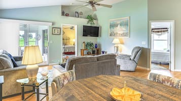 A living room with a wooden dining table, two sofas, a television, and a ceiling fan.