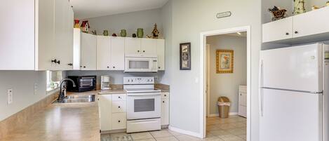 A kitchen with white cabinets, a microwave, an oven, a refrigerator, and a sink. There are decorative items on the cabinets and a rug on the floor.