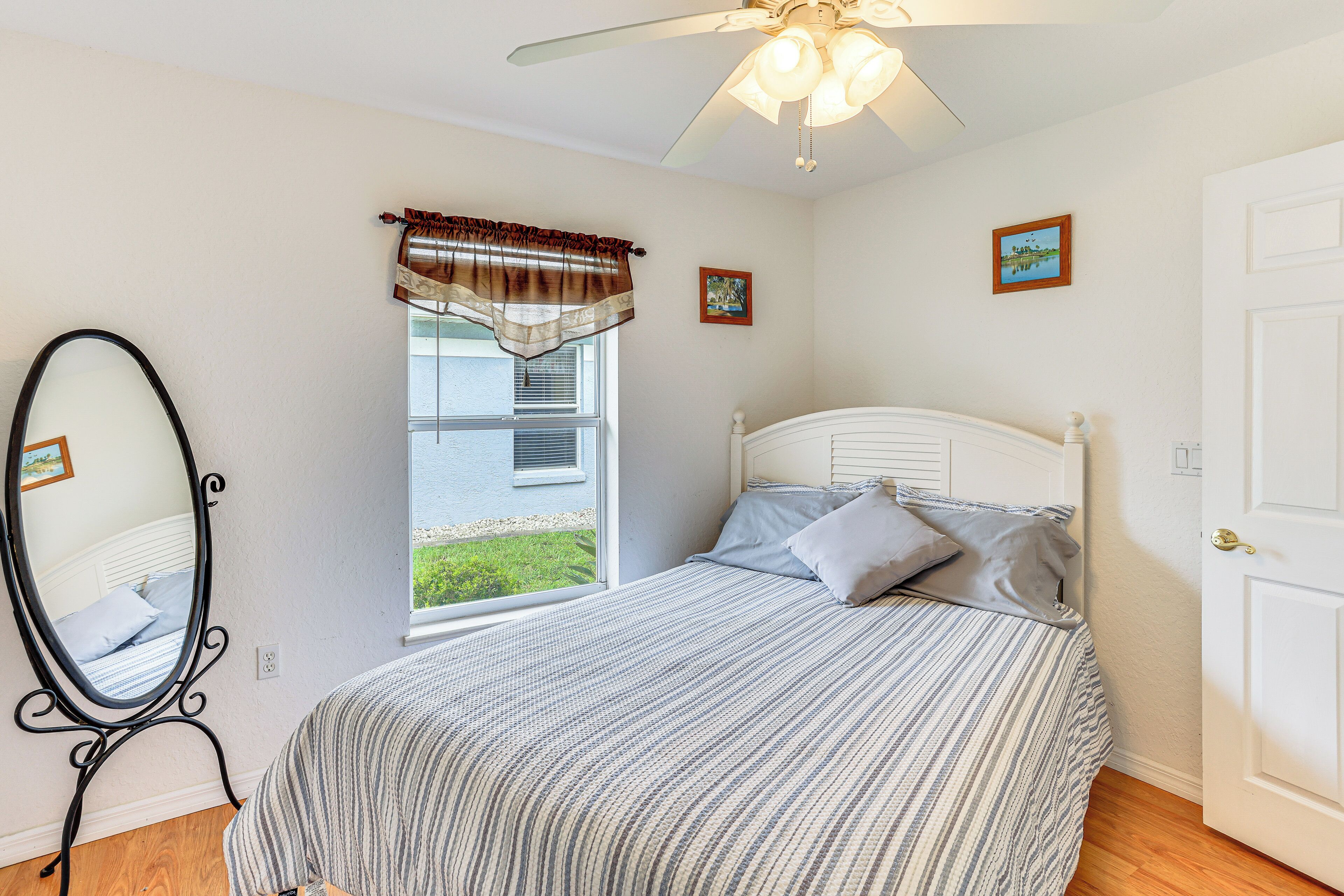 A bedroom with a bed, a window with curtains, a ceiling fan, and a door.