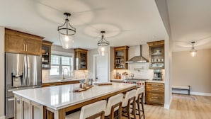 Una cocina amplia con una isla grande, armarios de madera y electrodomésticos de acero inoxidable, con iluminación colgante.