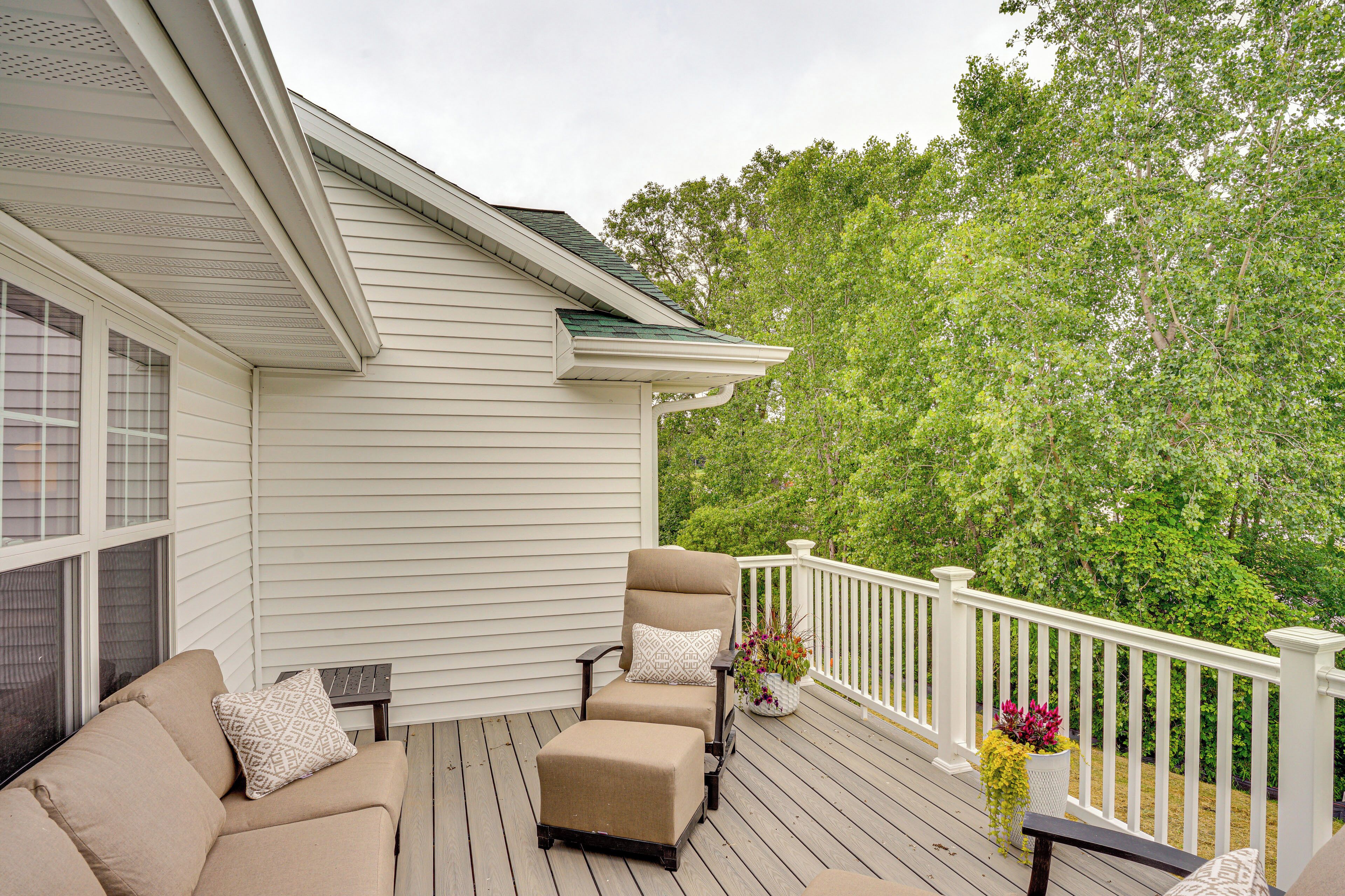 A covered deck with a beige sofa and armchair, a small table, and a white railing.