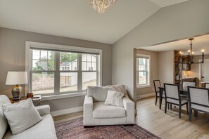 A spacious living room with a large window, a dining area with a chandelier, and a kitchen visible through an open doorway. - Walk to Beaches + Restaurants: Elkhart Lake Escape (Elkhart Lake)