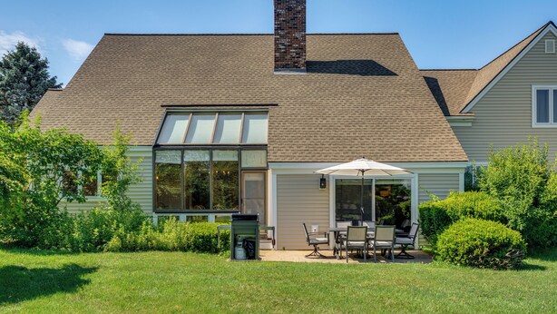 A house with a large garage door, a covered patio with outdoor furniture, and a brick chimney. - Lake & Beach Access: Family Townhome in Laconia (Laconia)