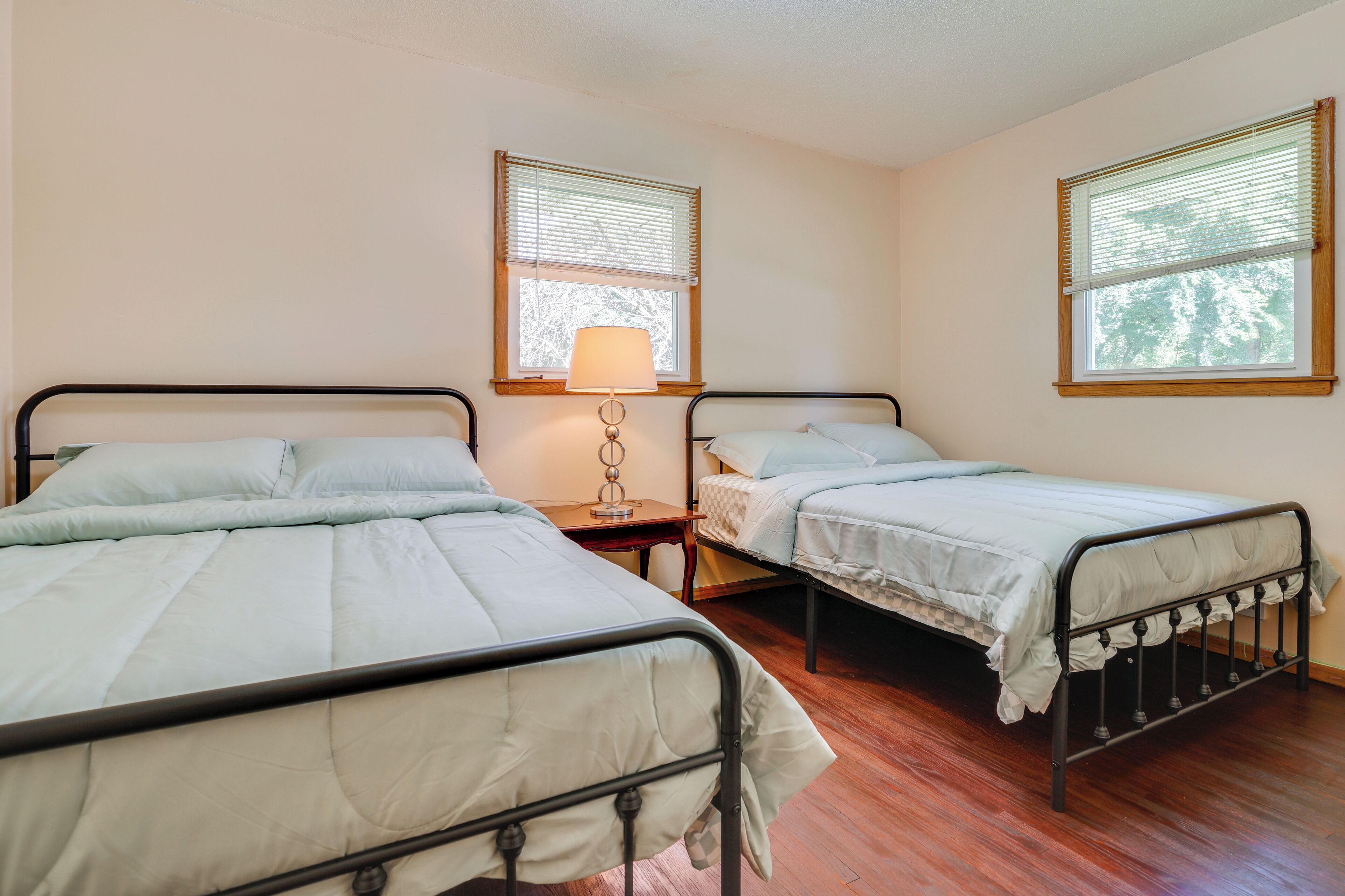 A room with two single beds, a nightstand with a lamp, and a window with blinds.