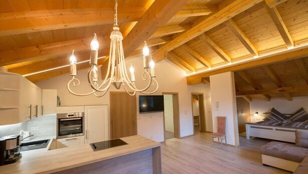 A spacious living area with a wooden ceiling, a central island with a built-in oven, a television, and a sofa. - Apartment 'Tscharfhof' with Mountain View and Private Terrace (San Leonardo in Passiria)