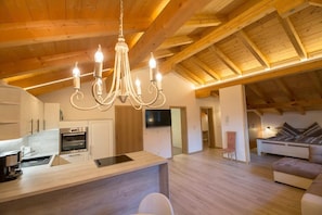 Un vaste espace de vie doté d’un plafond en bois, d’un îlot central avec un four encastré, d’une télévision et d’un canapé.