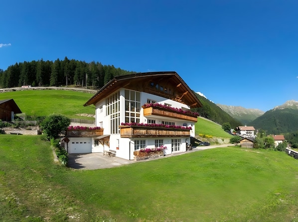 Un bâtiment à deux étages doté de balcons, entouré de champs verdoyants et de montagnes.