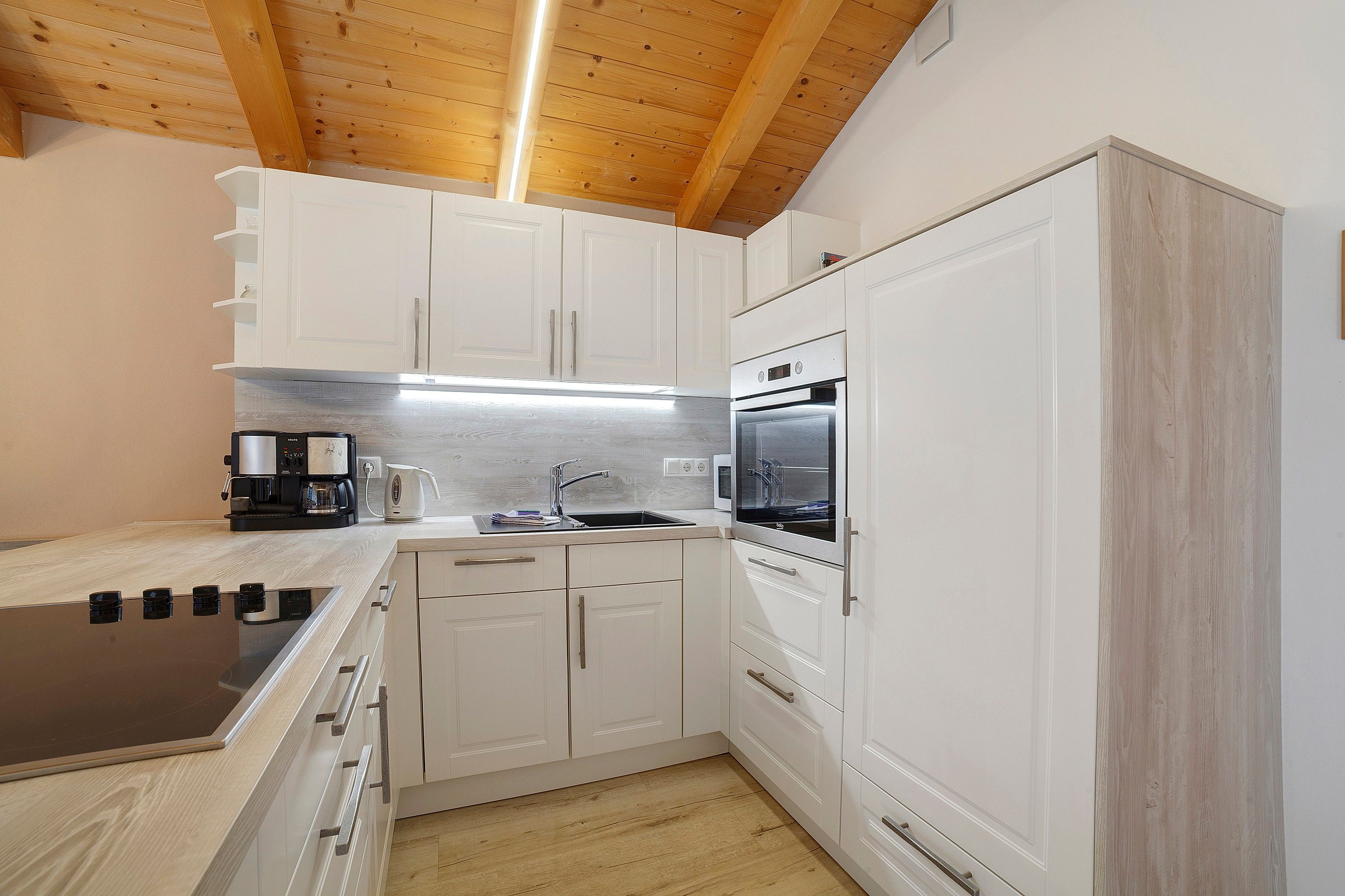 A compact kitchen with white cabinetry, a built-in oven, and a coffee maker.