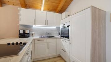 A compact kitchen with white cabinetry, a built-in oven, and a coffee maker.