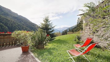 Ein Garten mit einem gepflasterten Weg, Blumentöpfen und zwei roten Stühlen.