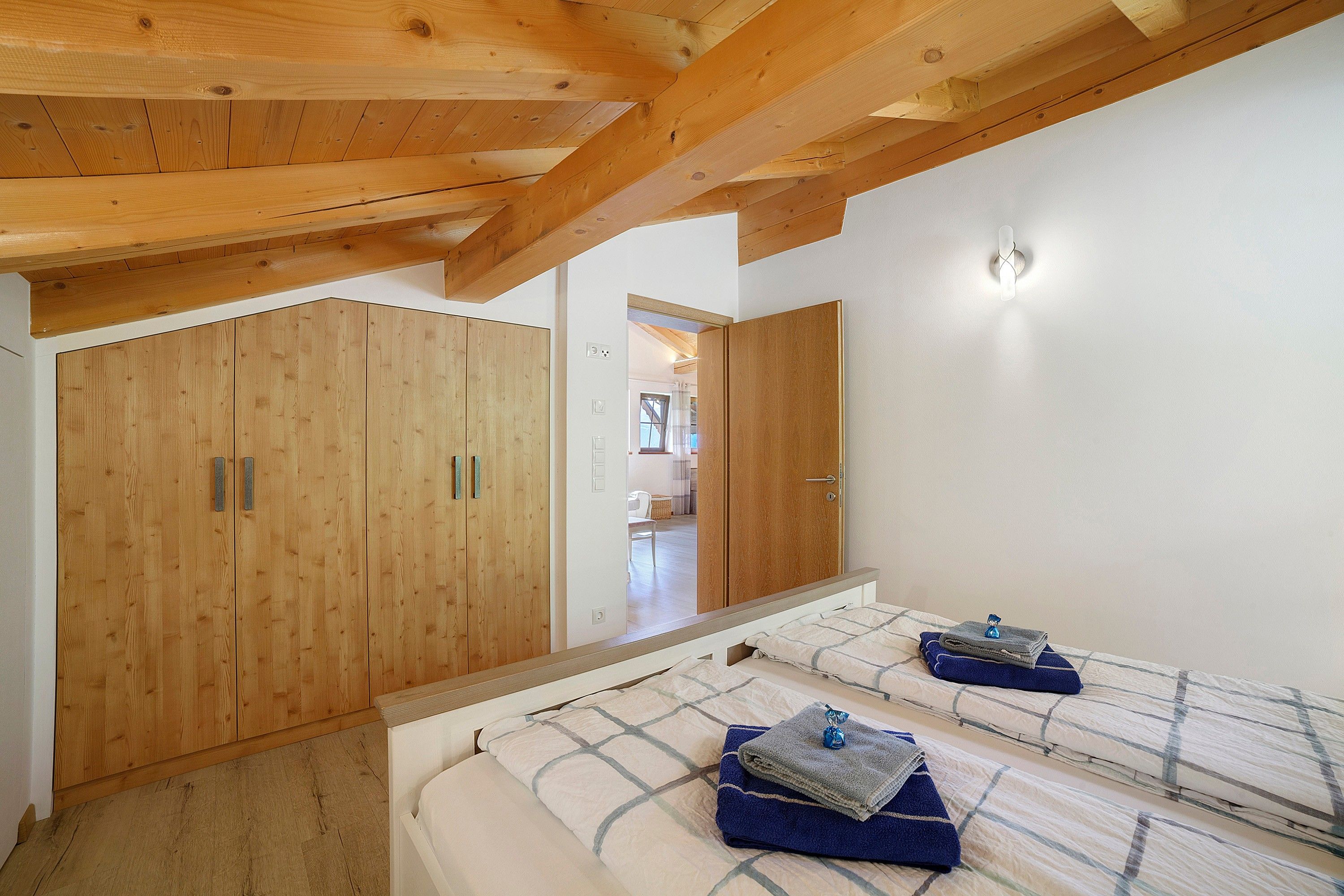 Ein Schlafzimmer mit Holzboden, einem Bett mit einem karierten Überwurf und einem Holzschrank.