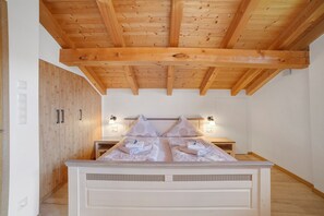 A bedroom with a wooden ceiling, a bed with a white headboard, two bedside tables, and a wardrobe.