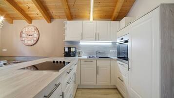 Una cocina moderna con vigas de madera, armarios blancos, horno empotrado y cafetera.