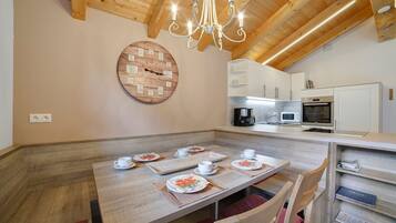 A dining area with a wooden table set for four, a chandelier, and a clock on the wall.
