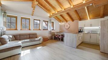 Un'ampia zona giorno con soffitto in legno, un divano, un tavolo da pranzo con sedie e una cucina con mobili bianchi.