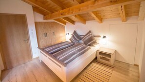 A bedroom with a bed, wooden ceiling beams, a nightstand, and a door. - Apartment 'Tscharfhof' with Mountain View and Private Terrace (San Leonardo in Passiria)
