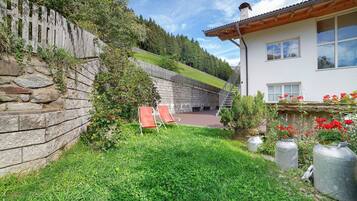 Un mur de pierre, une clôture en bois, une zone herbeuse et un bâtiment avec un escalier.