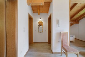 Un pasillo con vigas de madera, un espejo, una lámpara y una silla.