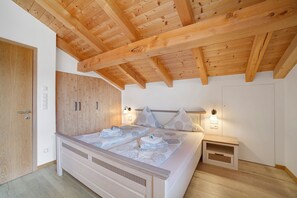 A bedroom with a wooden ceiling, a bed with pillows, a nightstand, and a wardrobe.