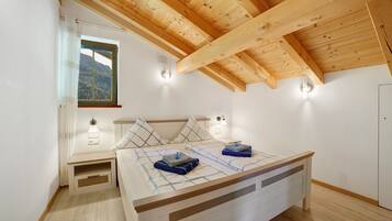 A bedroom with a wooden ceiling, a bed with a headboard, bedside lamps, and a window with a view of a forest.