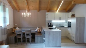 A modern kitchen with wooden beams, a built-in island, and a dining area with a bench and chairs. - Apartment 'Tscharfhof' with Mountain View and Private Terrace (San Leonardo in Passiria)